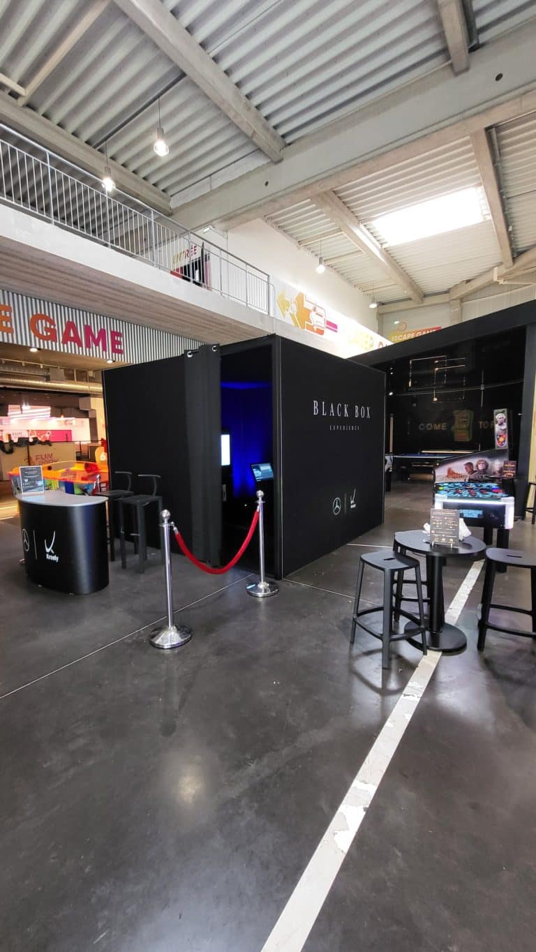 Black Box Experience Mercedes-Benz Kroely dans un complexe de loisirs, rideau ouvert sur l'intérieur bleu, comptoir d'accueil et cordon rouge
