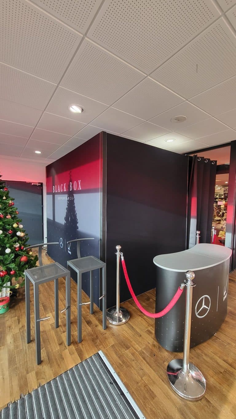 Black Box Experience Mercedes-Benz Kroely éclairée en rouge, avec comptoir d'accueil, tabourets hauts et sapin de Noël