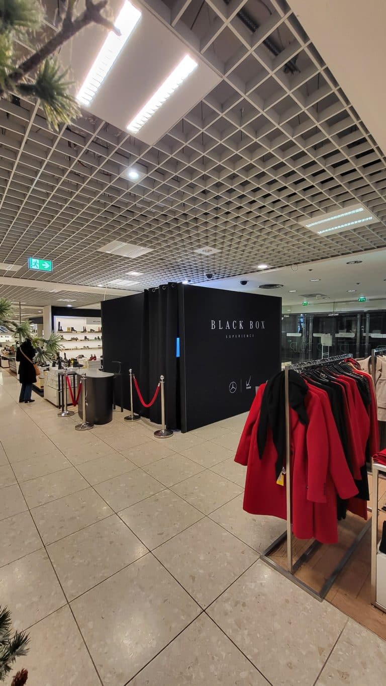 Cabine Black Box Experience aux logos Mercedes-Benz et Kroely installée dans un grand magasin de Nancy, avec comptoir d'accueil et potelets à cordon rouge