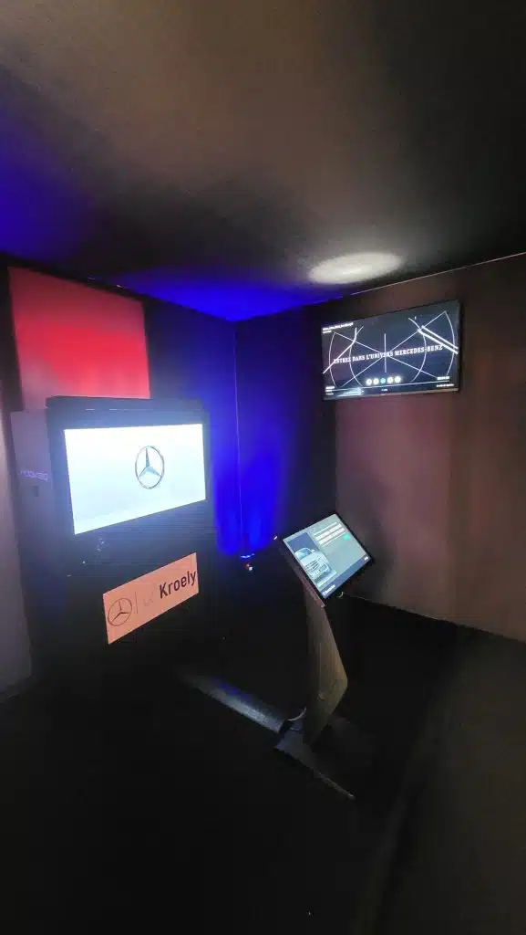 Intérieur noir de la Black Box : box hologramme avec l'étoile Mercedes, écran mural « Entrez dans l'univers Mercedes-Benz » et borne tactile sous un éclairage bleu