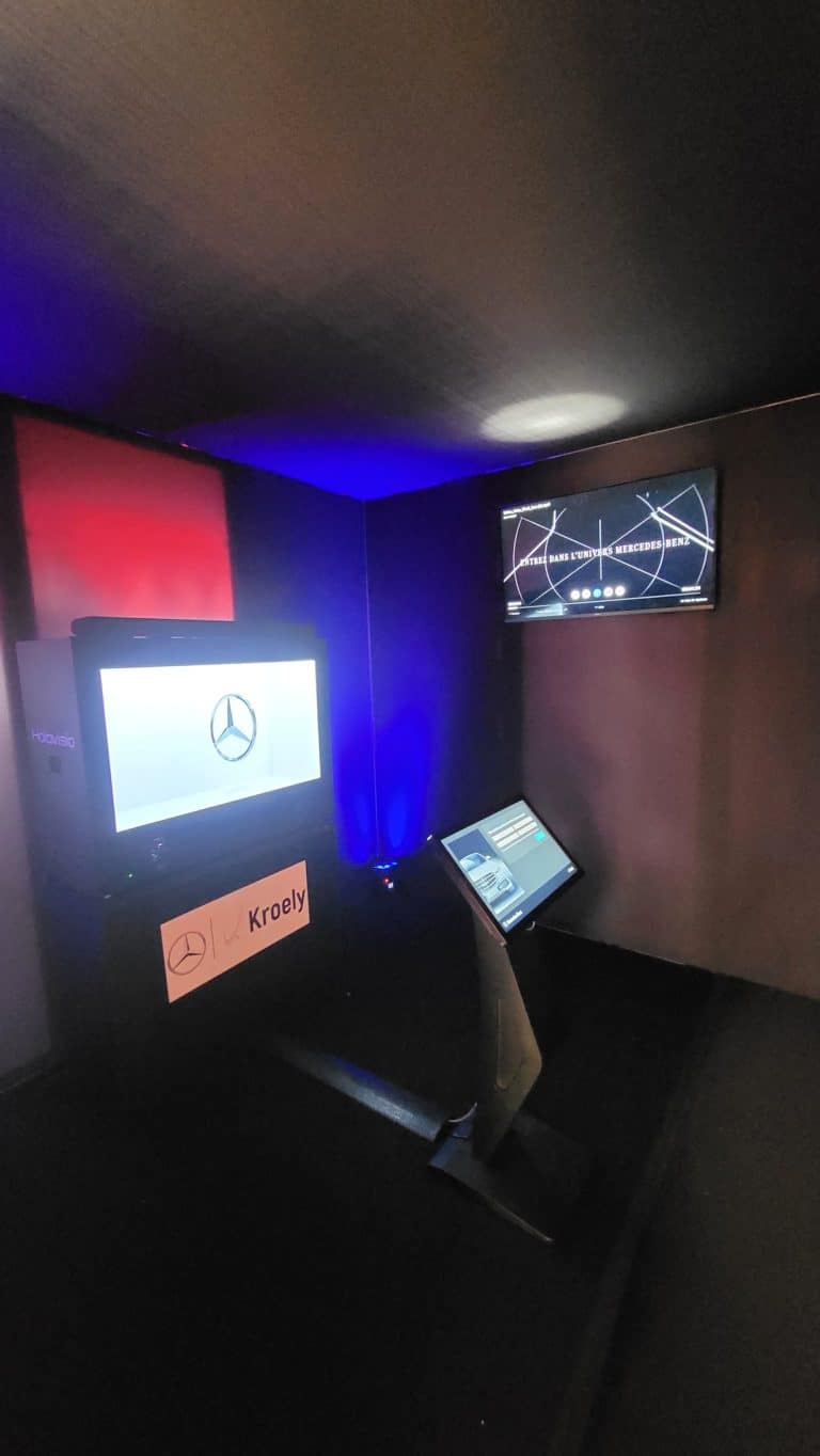 Intérieur noir de la Black Box : box hologramme avec l'étoile Mercedes, écran mural « Entrez dans l'univers Mercedes-Benz » et borne tactile sous un éclairage bleu