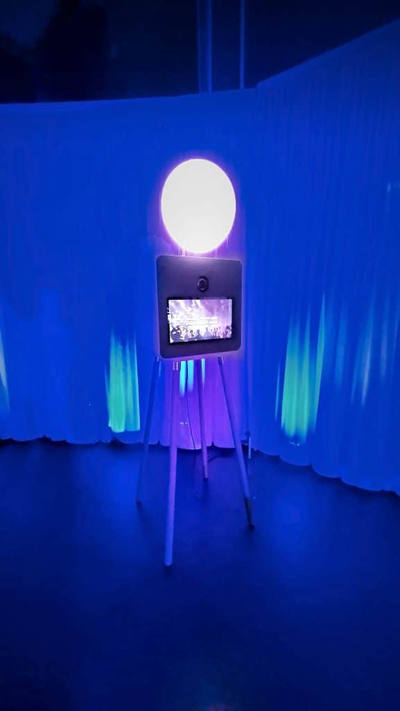 Borne selfie ONE et son flash annulaire devant des tentures bleues, en soirée