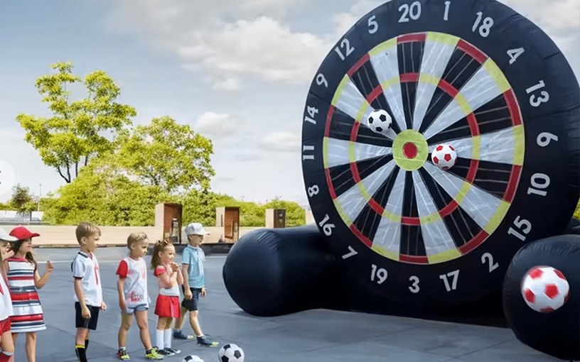 Enfants en file devant une cible gonflable géante, ballons à velcro au sol