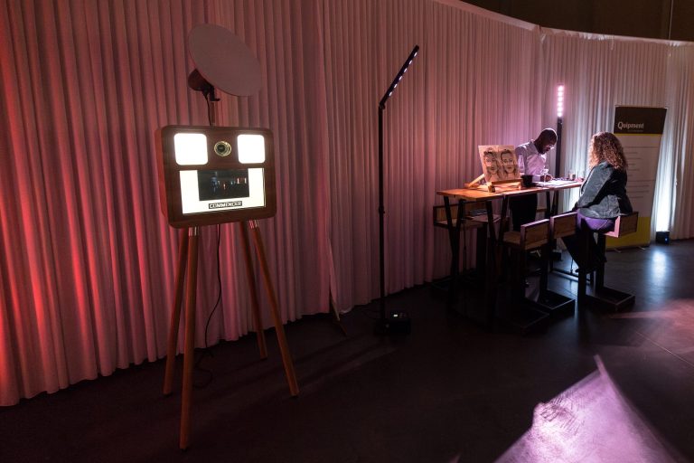 Borne selfie ONE devant une tenture rose, table de tirages à côté