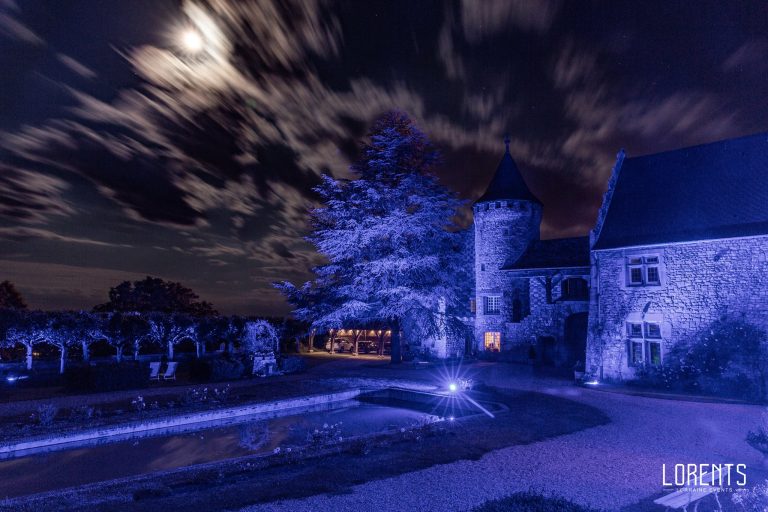 Tour et façade du château d’Hattonchâtel mises en lumière en bleu par LORENTS, nuages filant sous la lune