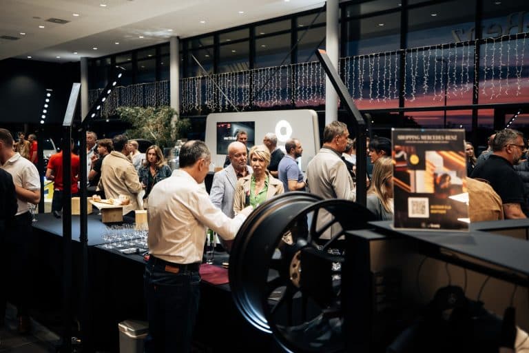 Invités autour du buffet du showroom Mercedes Kroely, jante exposée au premier plan, tubes LED verticaux en arrière-plan
