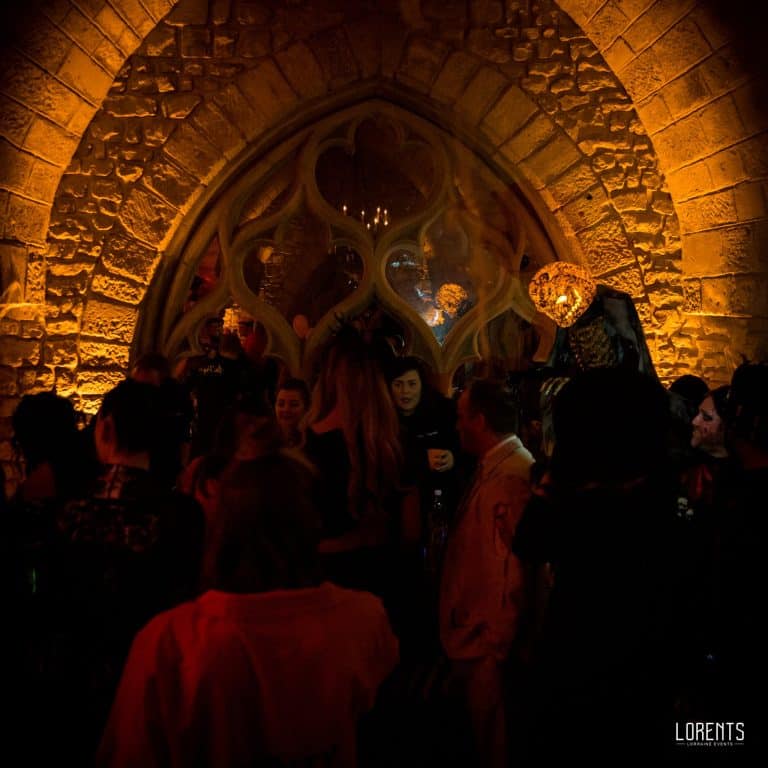 Cave voûtée du château d’Hattonchâtel éclairée en ambre et décorée par LORENTS pour une soirée d’Halloween, invités sous l’arche gothique