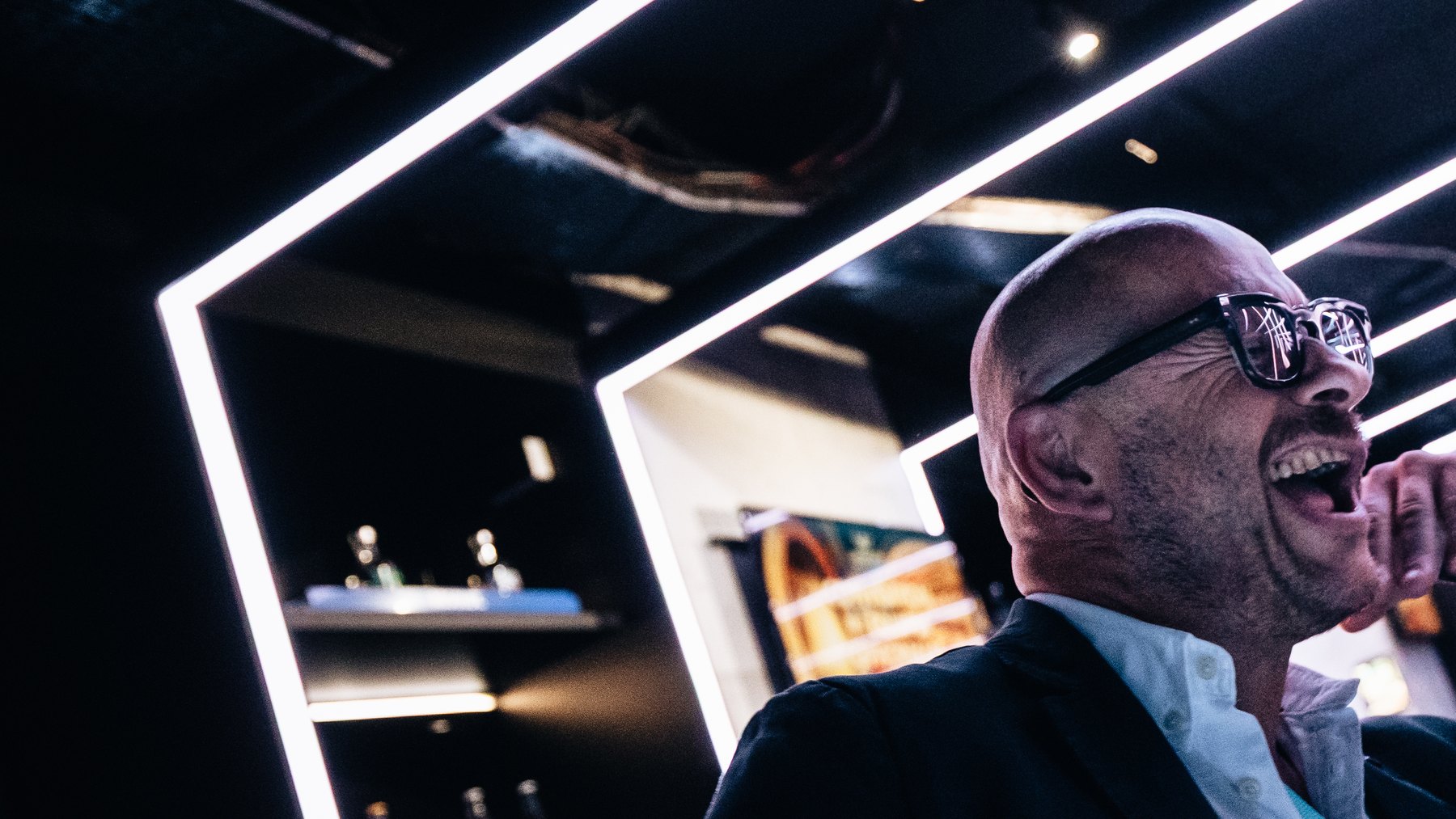 Un invité éclate de rire au bar néon du Rex Club à Paris, pendant une convention d'entreprise