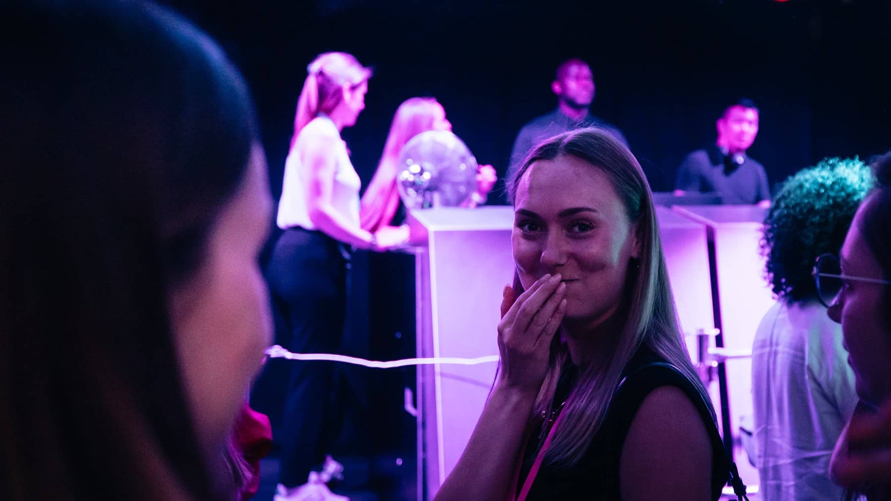 Une participante sourit, la main devant la bouche, sous la lumière violette d'une soirée d'entreprise