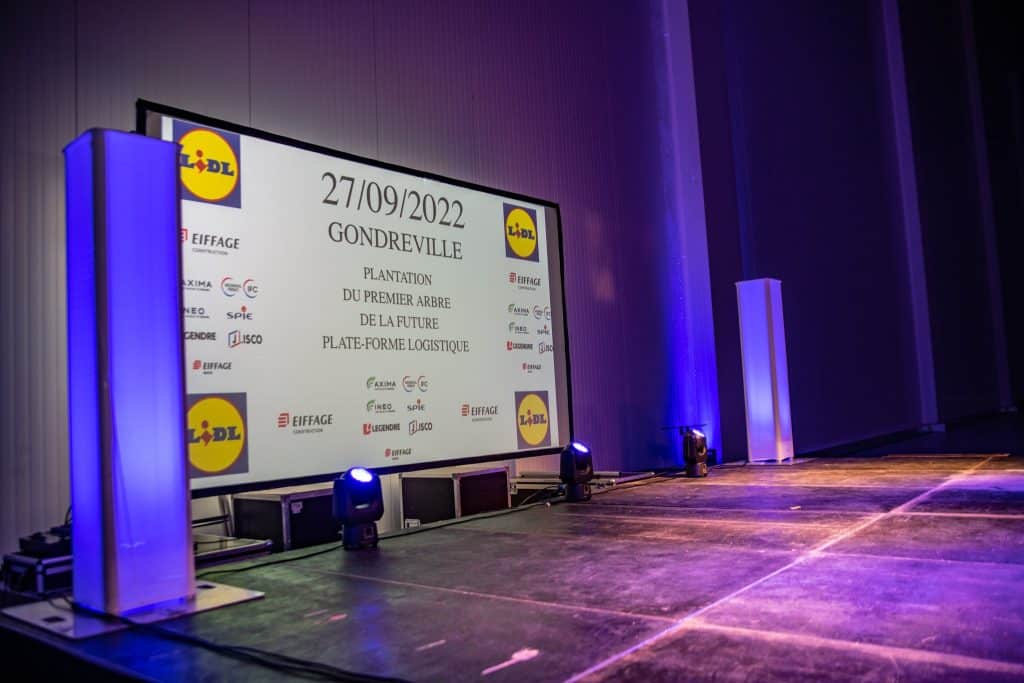 Écran de projection au visuel de la journée Lidl et Eiffage, colonnes lumineuses et lyres sur la scène