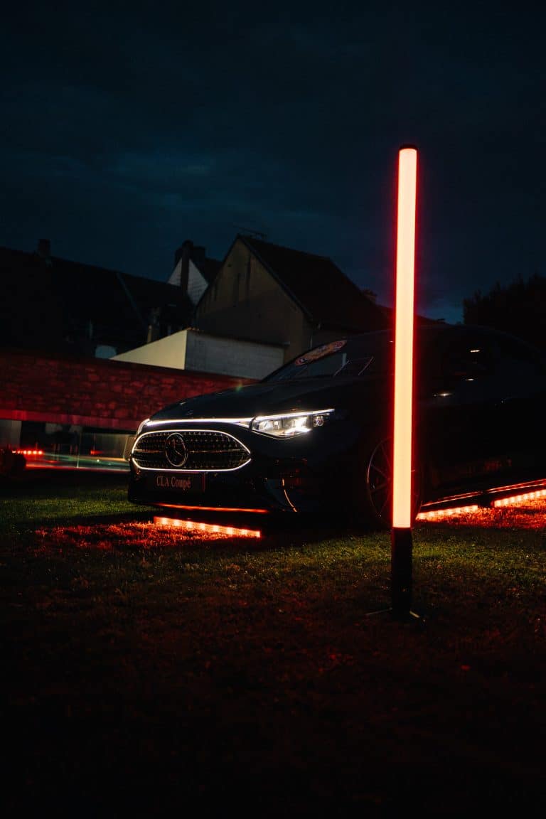 Mercedes CLA Coupé noire de nuit sur la pelouse, soulignée par des barres LED au sol et un tube LED Pixtube vertical
