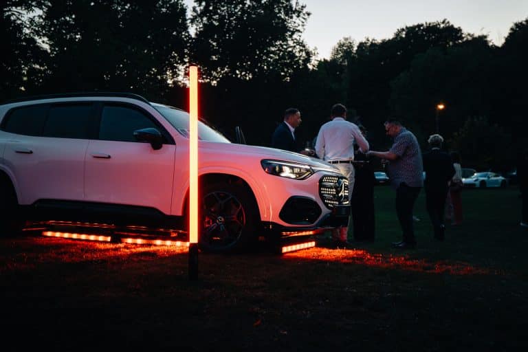 Invités discutant autour d'un Mercedes GLB blanc éclairé par des barres LED au sol et un tube LED Pixtube, à la tombée du jour