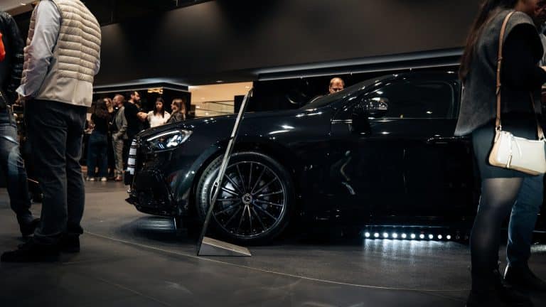 Mercedes noire de profil dans le showroom, barre LED bleue posée au sol sous le bas de caisse, invités autour