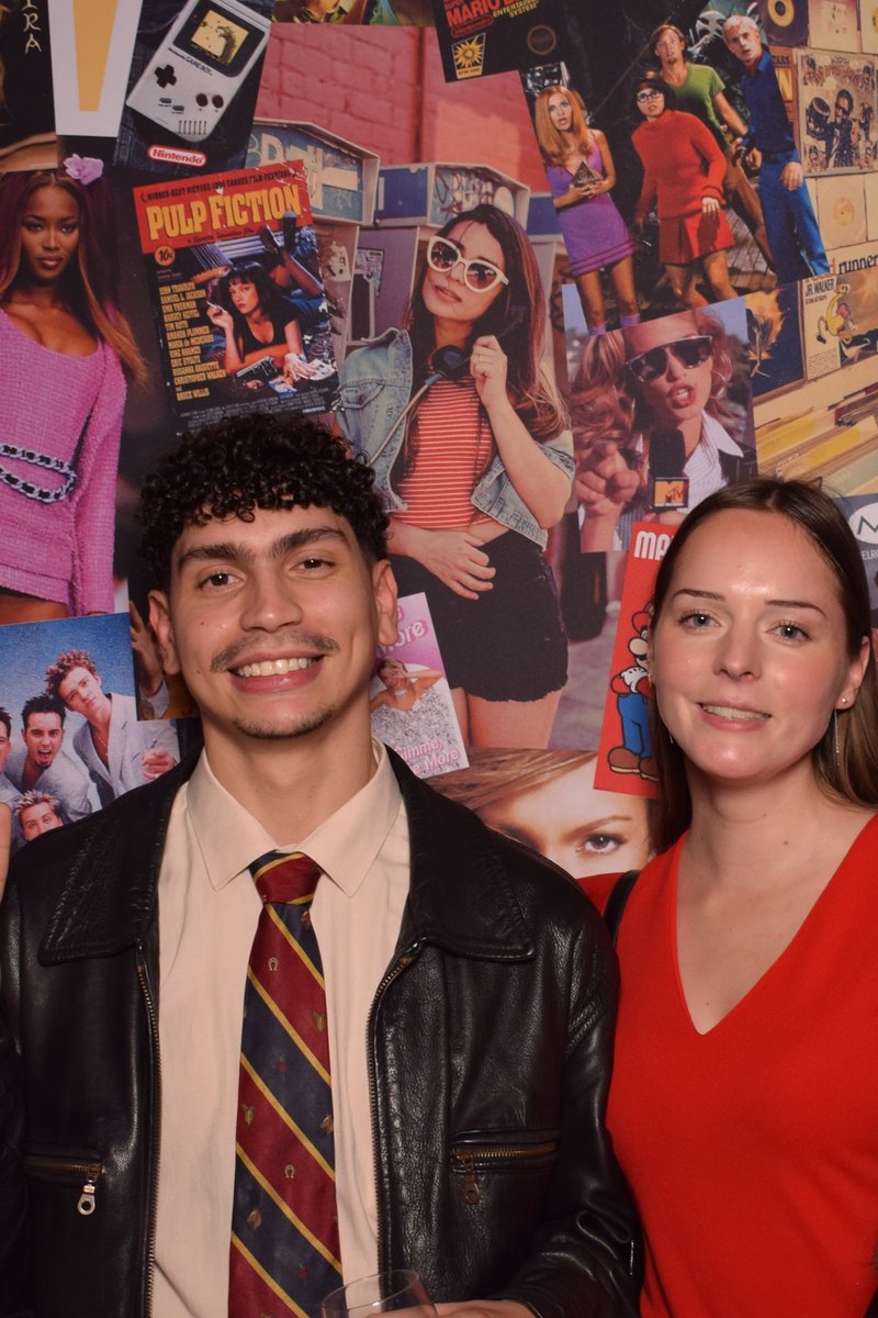 Un invité en cravate et une invitée en rouge devant le mur photo