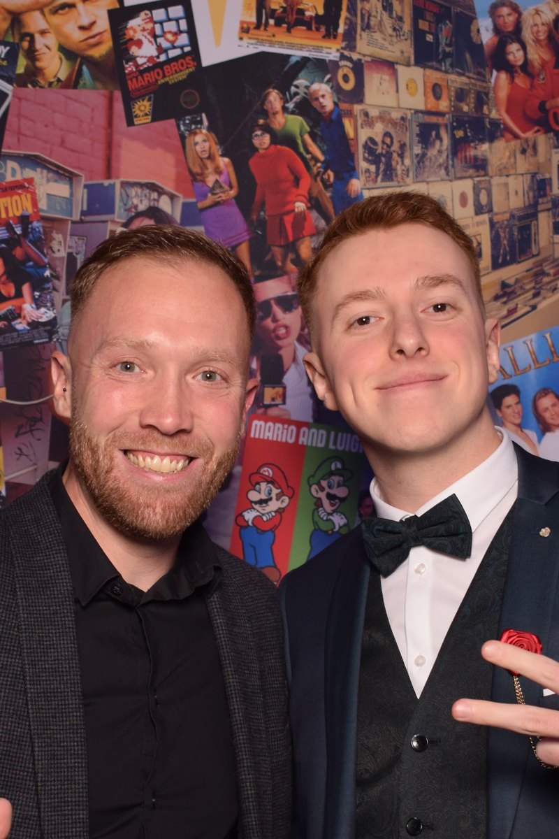 Deux invités en smoking posent devant le fond années 90 du photocall