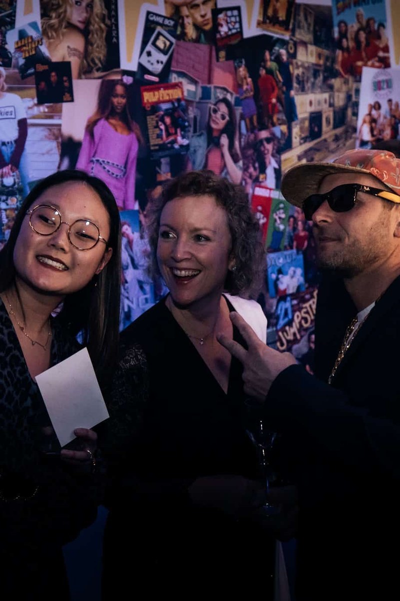 Trois invités devant le mur d’affiches années 90 pendant un selfie