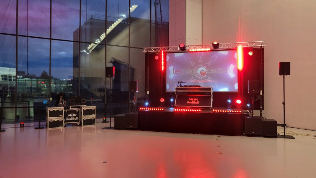 Scène DJ des Négociales devant la verrière, ciel rose du crépuscule, écran LED et éclairage rouge