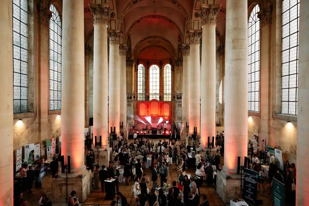 Vue plongeante de la nef de l'abbaye des Prémontrés remplie de participants pendant une convention, colonnes éclairées en rouge et scène au fond