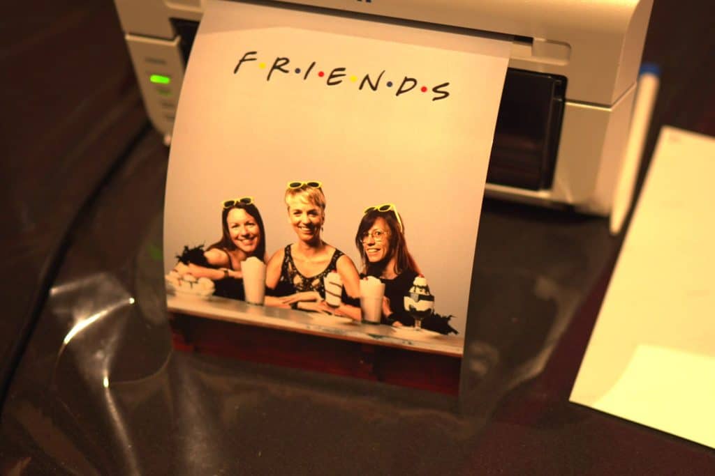 Tirage façon affiche Friends de trois invitées, posé devant l'imprimante du stand photo