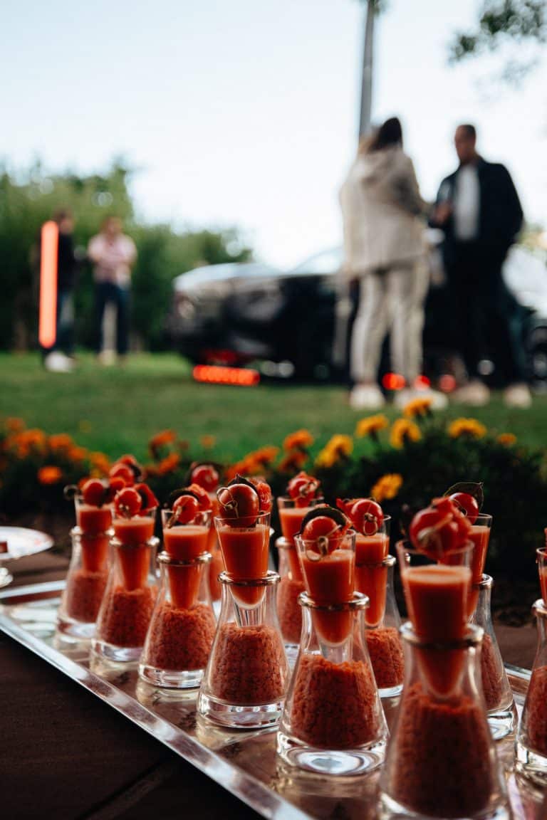 Verrines du cocktail dînatoire au premier plan, invités et Mercedes éclairée en arrière-plan dans le jardin de l'Auberge Saint-Walfrid