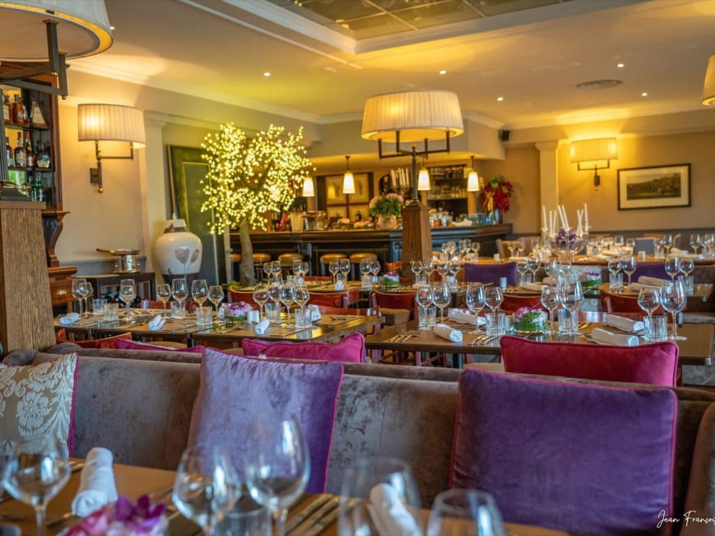 Salle du restaurant dressée pour une réception, banquettes à coussins violets et arbre lumineux
