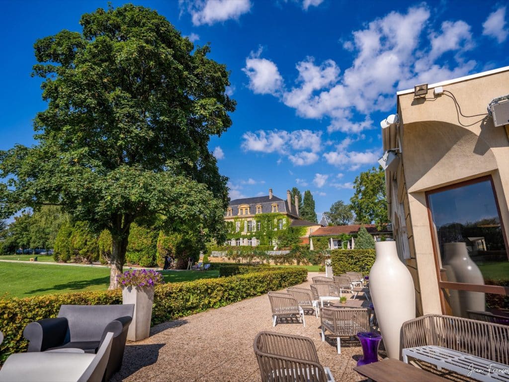 Terrasse du club-house et ses salons de jardin, le château en arrière-plan, à Marly